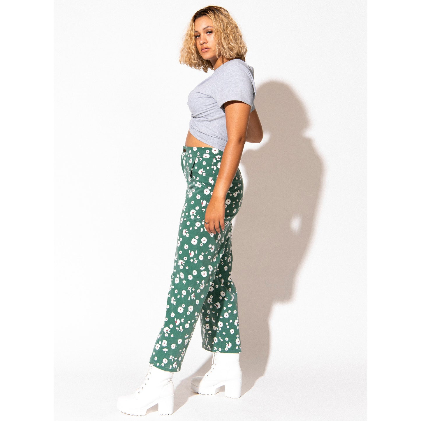 Person wearing a light gray crop top and green floral pants against a white background