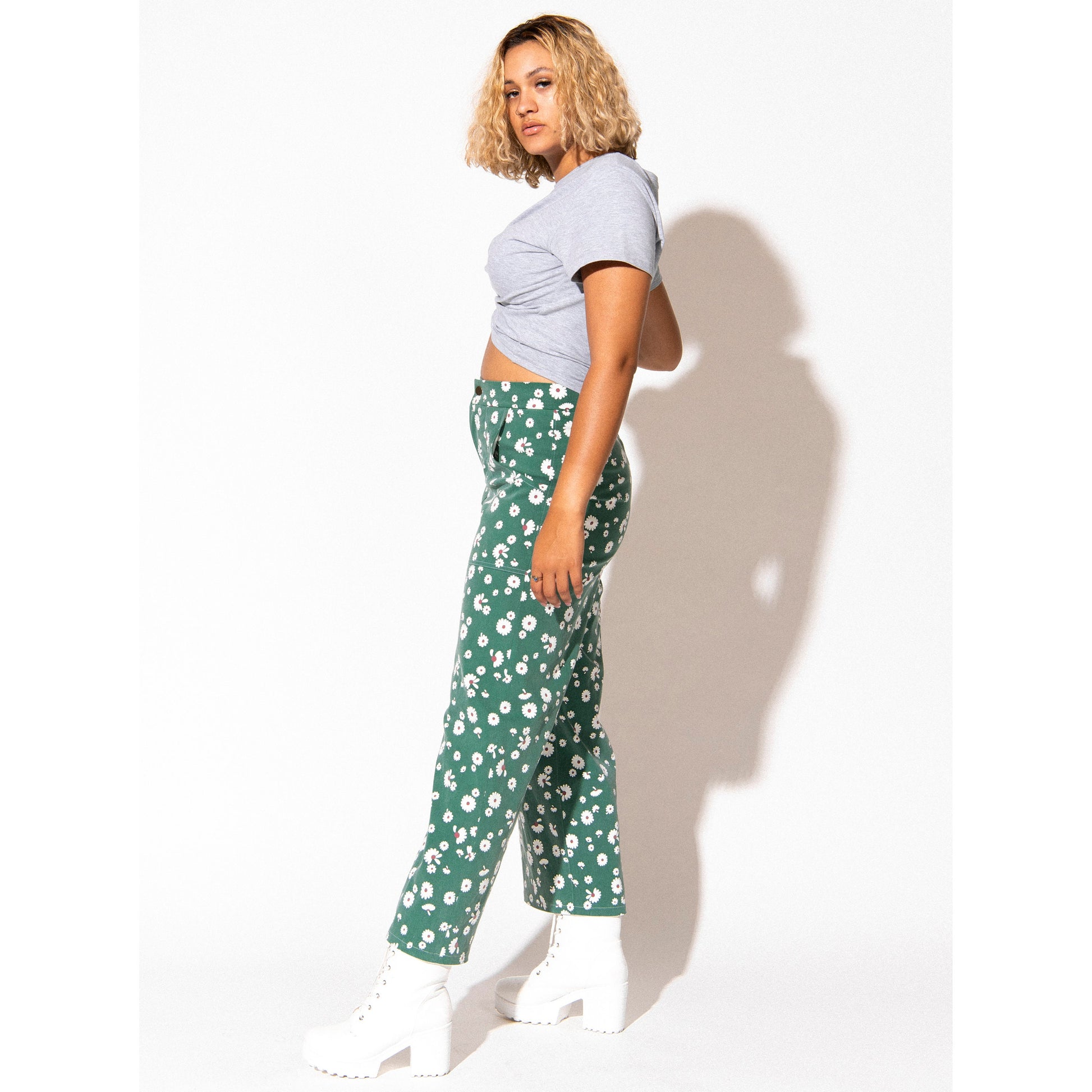Person wearing a light gray crop top and green floral pants against a white background