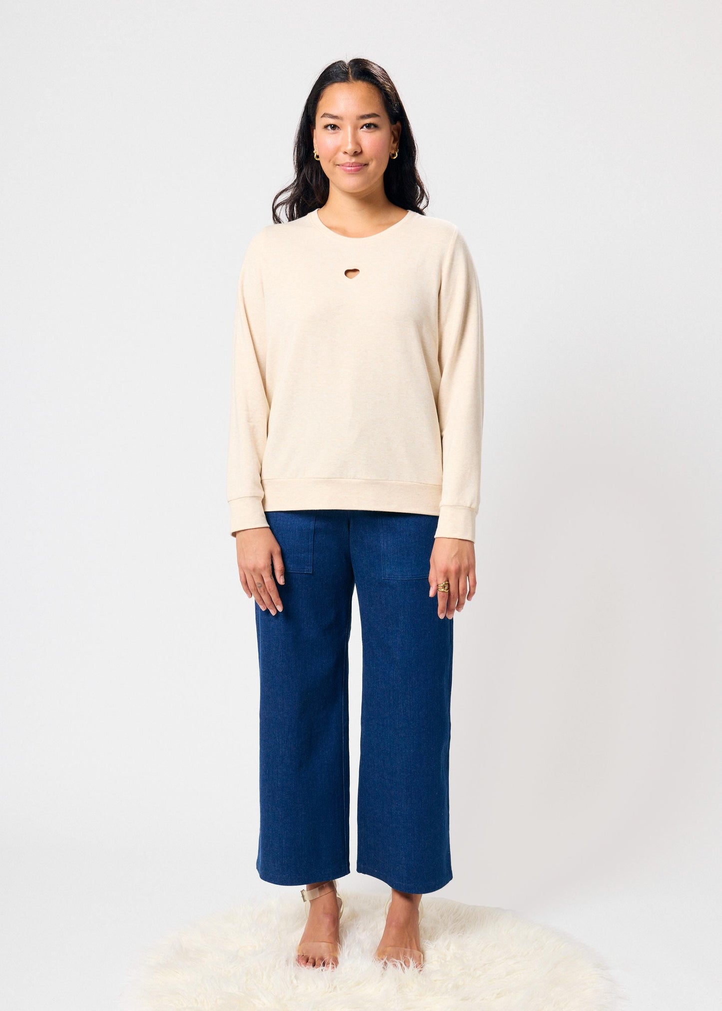 Woman wearing a beige sweatshirt and blue jeans on a white background