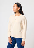 Woman wearing a beige sweatshirt with a heart cut out and blue pants on a white background