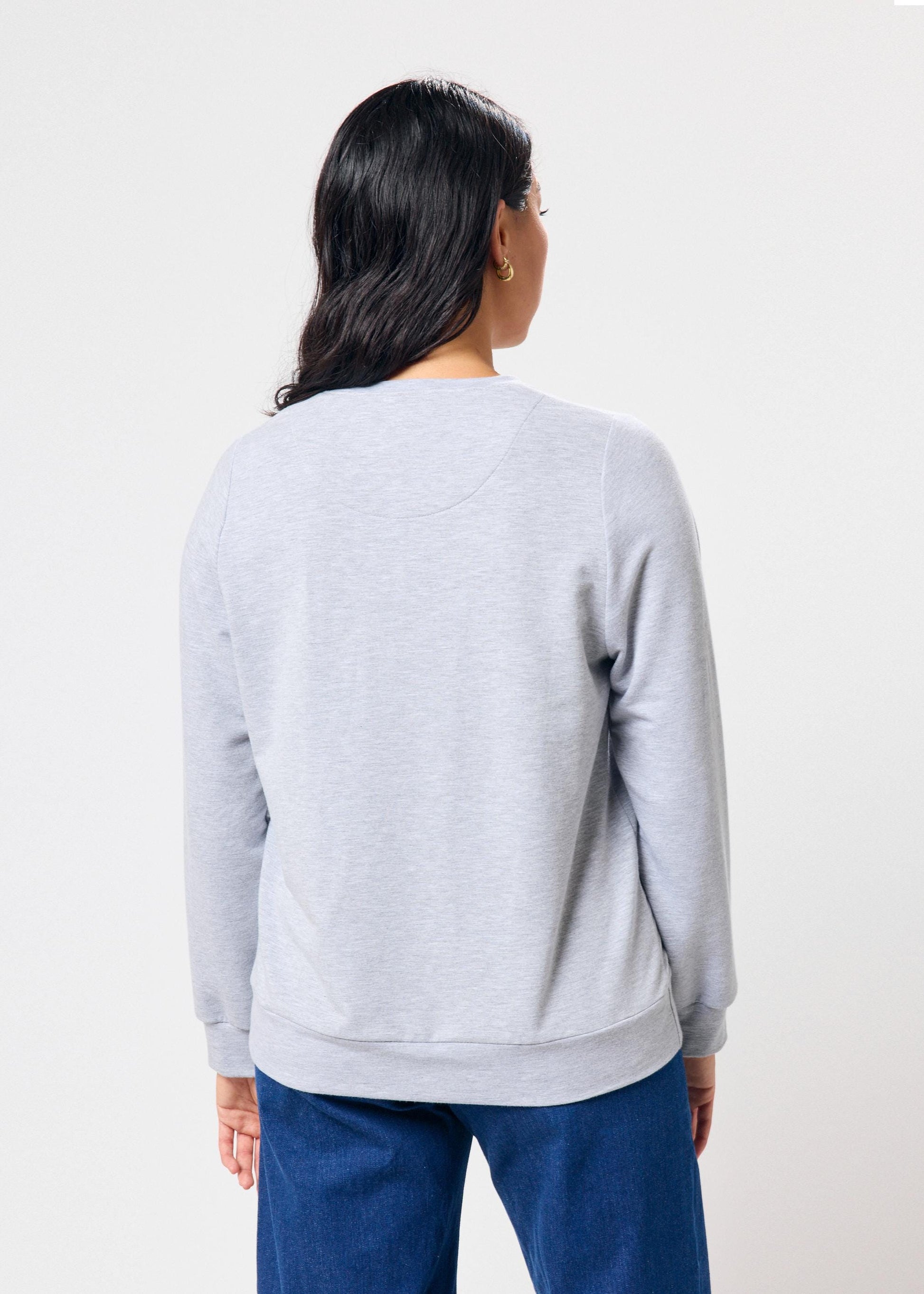 Person wearing a light gray sweatshirt and blue pants on a white background