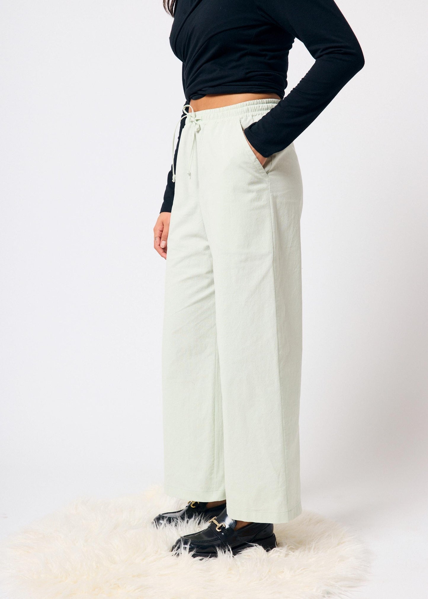 Person wearing pale green pants and black shoes on a white background