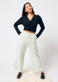 Woman wearing a black top and pale green pants on a white background
