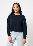 Woman wearing cropped black long sleeve tee shirt with embroidered gray barbed wire design on left arm