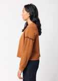 Woman wearing a brown long-sleeve top with embroidered black barbed wire detail on sleeve on a white background