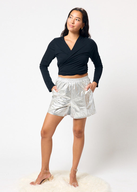 Woman wearing a black long-sleeve top and silver shorts on a white background