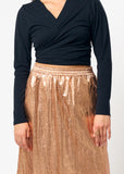 Person wearing a black long-sleeve top and bronze skirt on a white background