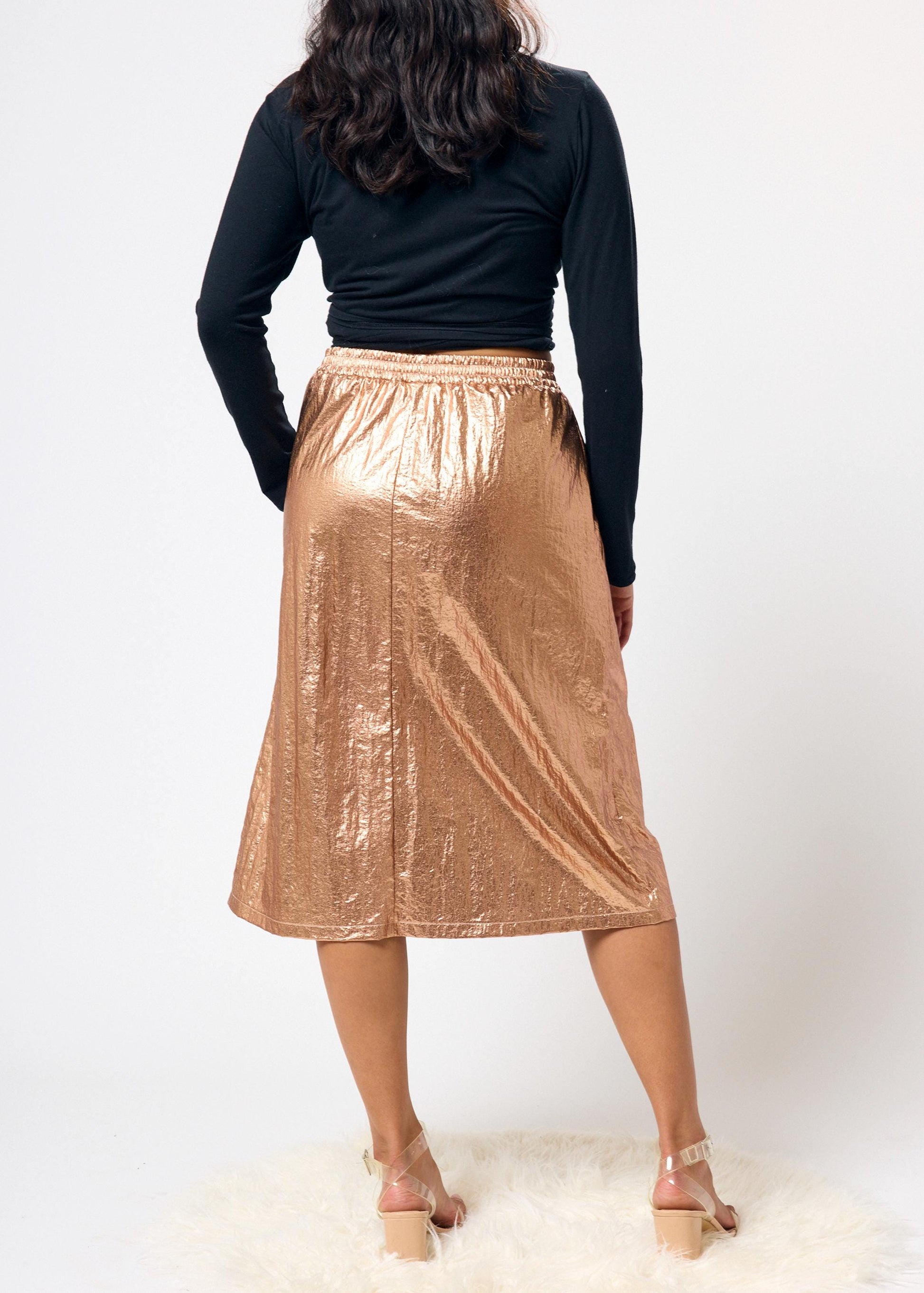 Person wearing a black top and bronze metallic skirt on a white background