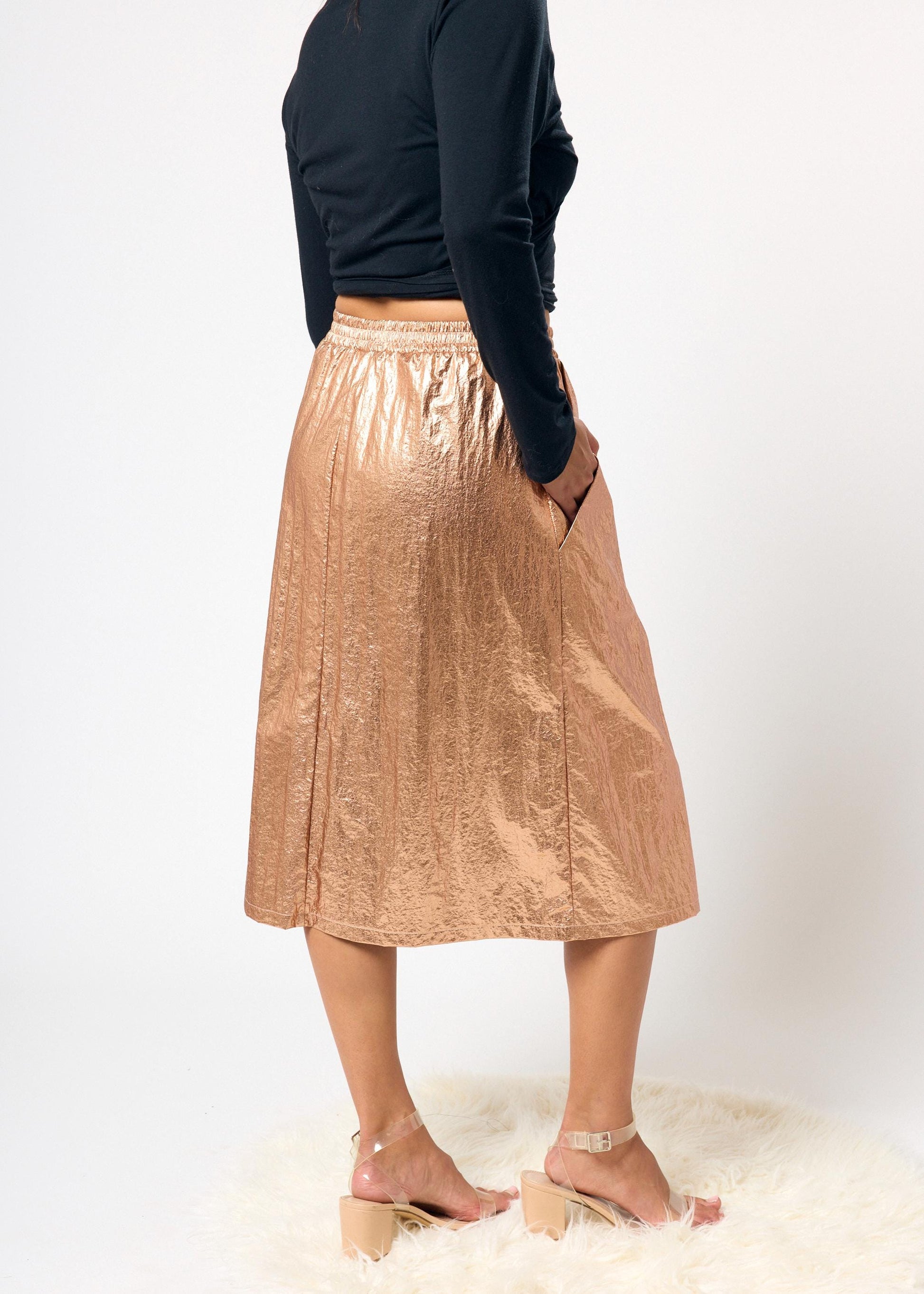 Person wearing a black top and bronze metallic skirt on a white background
