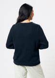 Person wearing a black sweater and white pants on a light gray background