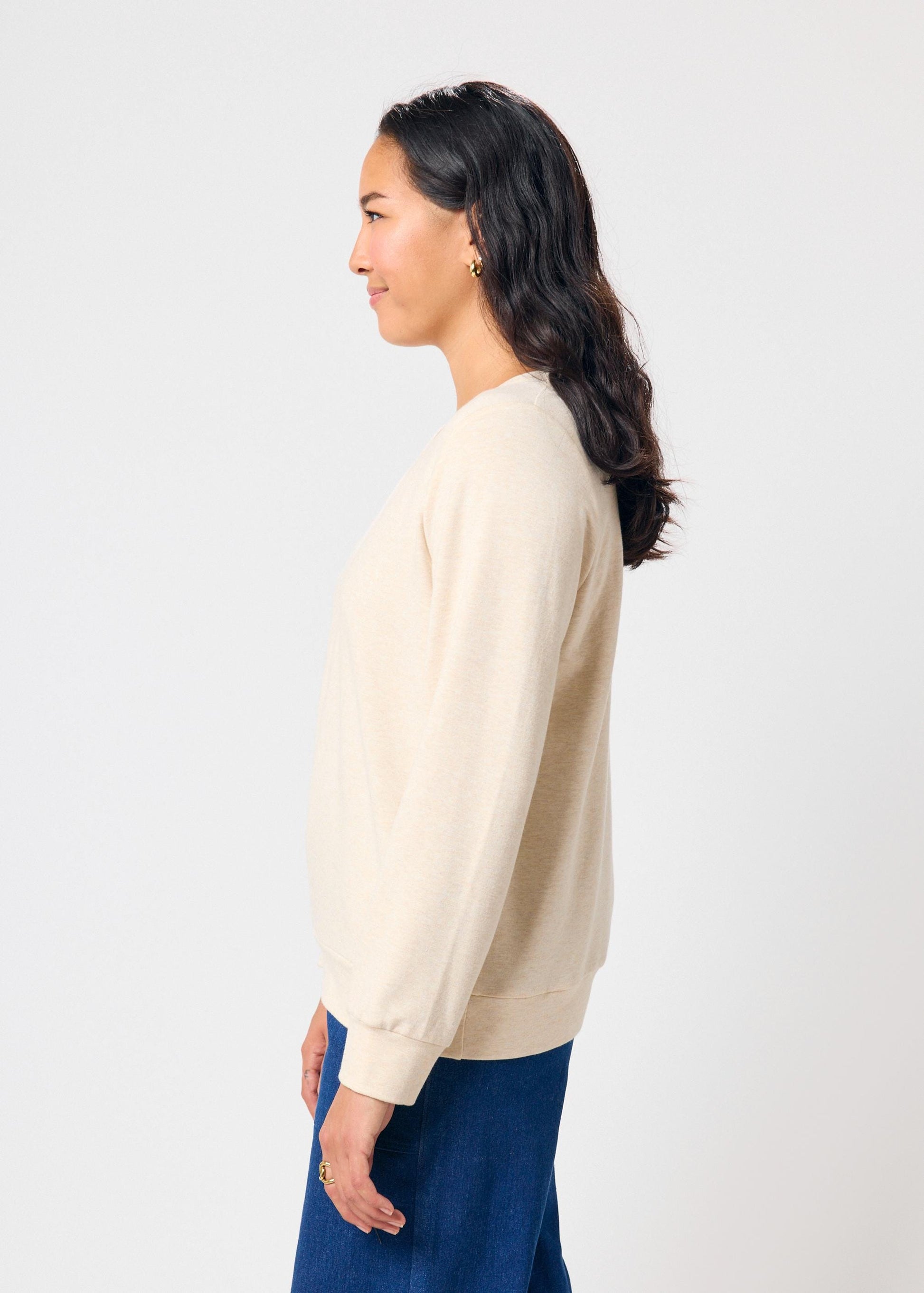 Woman wearing a beige sweatshirt and blue pants against a white background