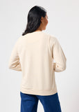 Woman wearing a beige sweatshirt and blue pants on a white background