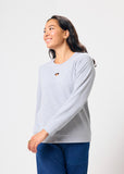 Woman wearing a light gray sweatshirt with a heart cut out and blue pants against a white background