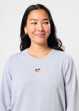 Person wearing a light gray sweatshirt with a heart design on a plain background