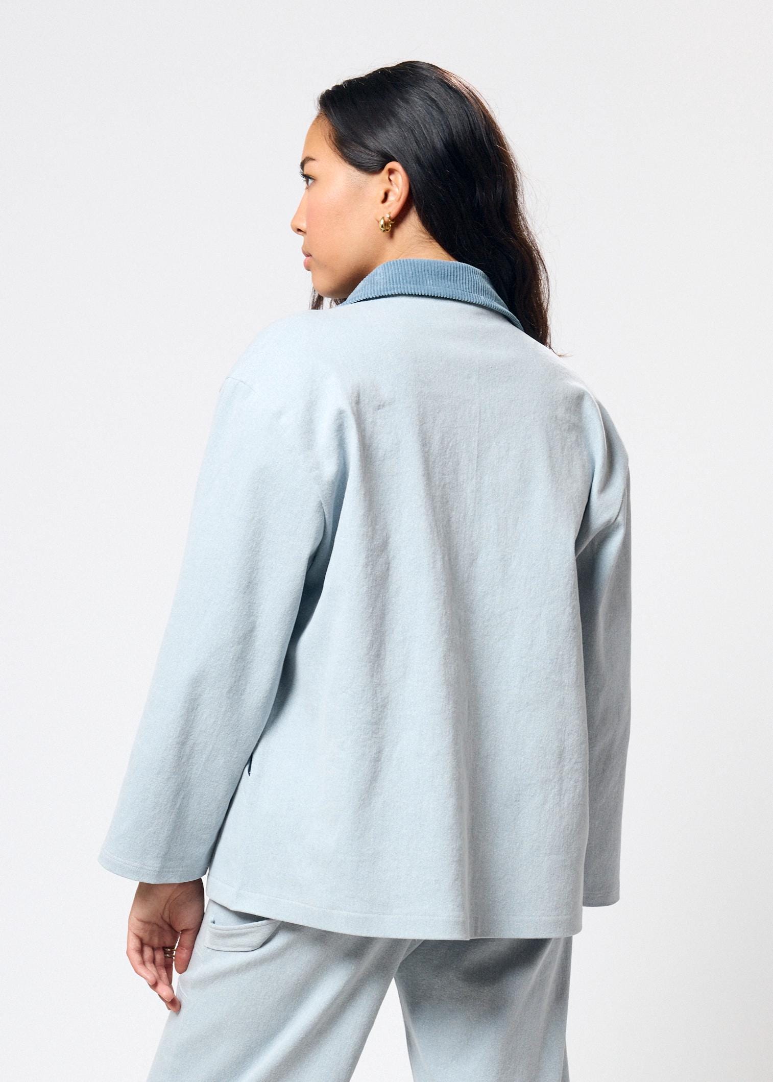 Person wearing a light blue jacket and pants on a white background