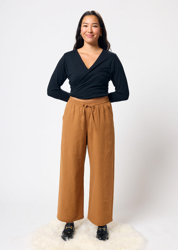 Woman wearing a black top and tan wide-leg pants on a white background