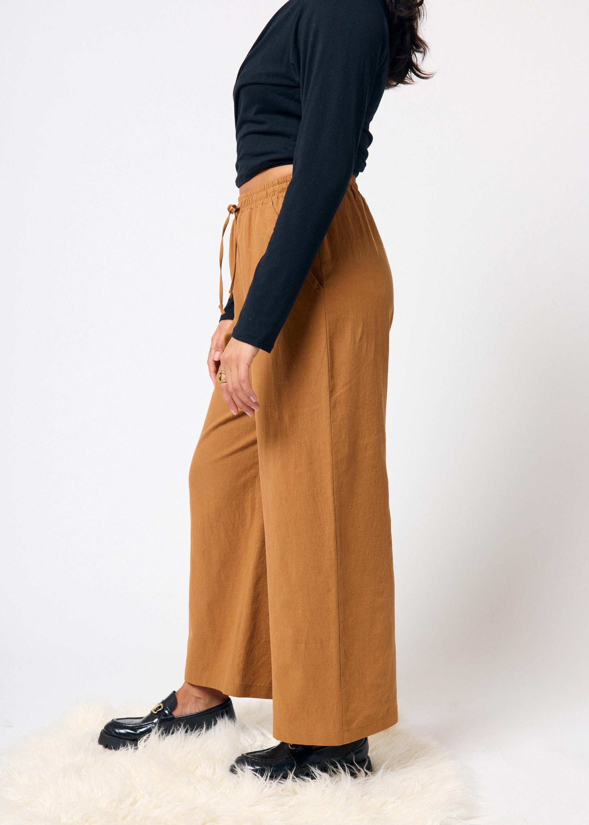 Person wearing mustard yellow wide-leg pants and a black top on a white background