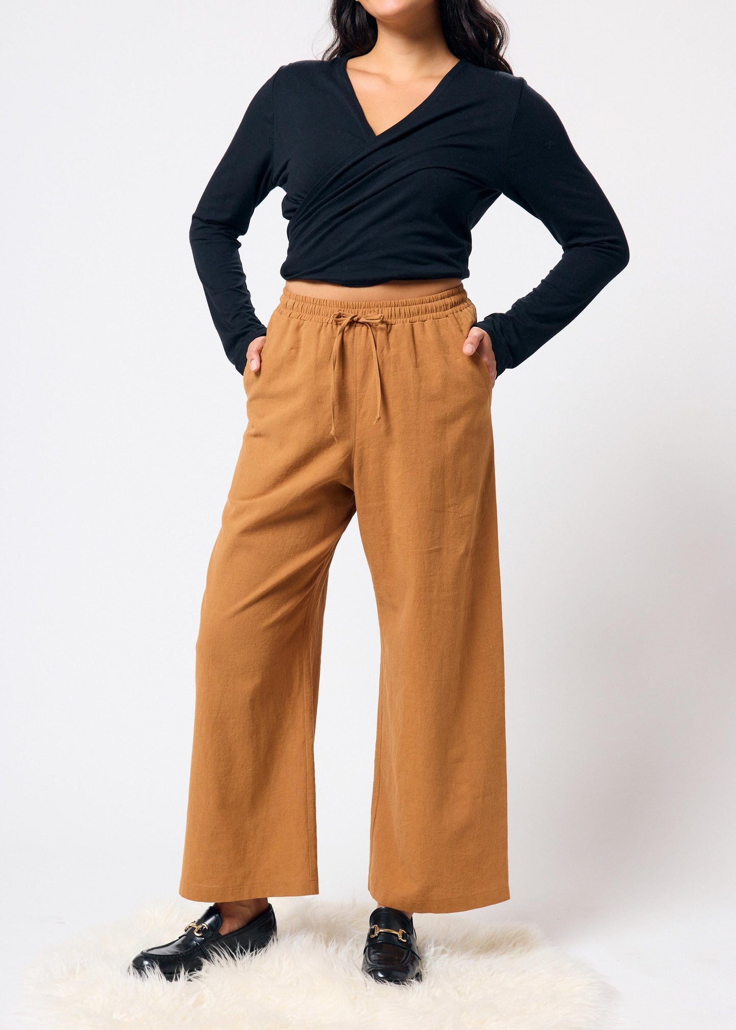 Person wearing a black long-sleeve top and tan wide-leg pants on a white background