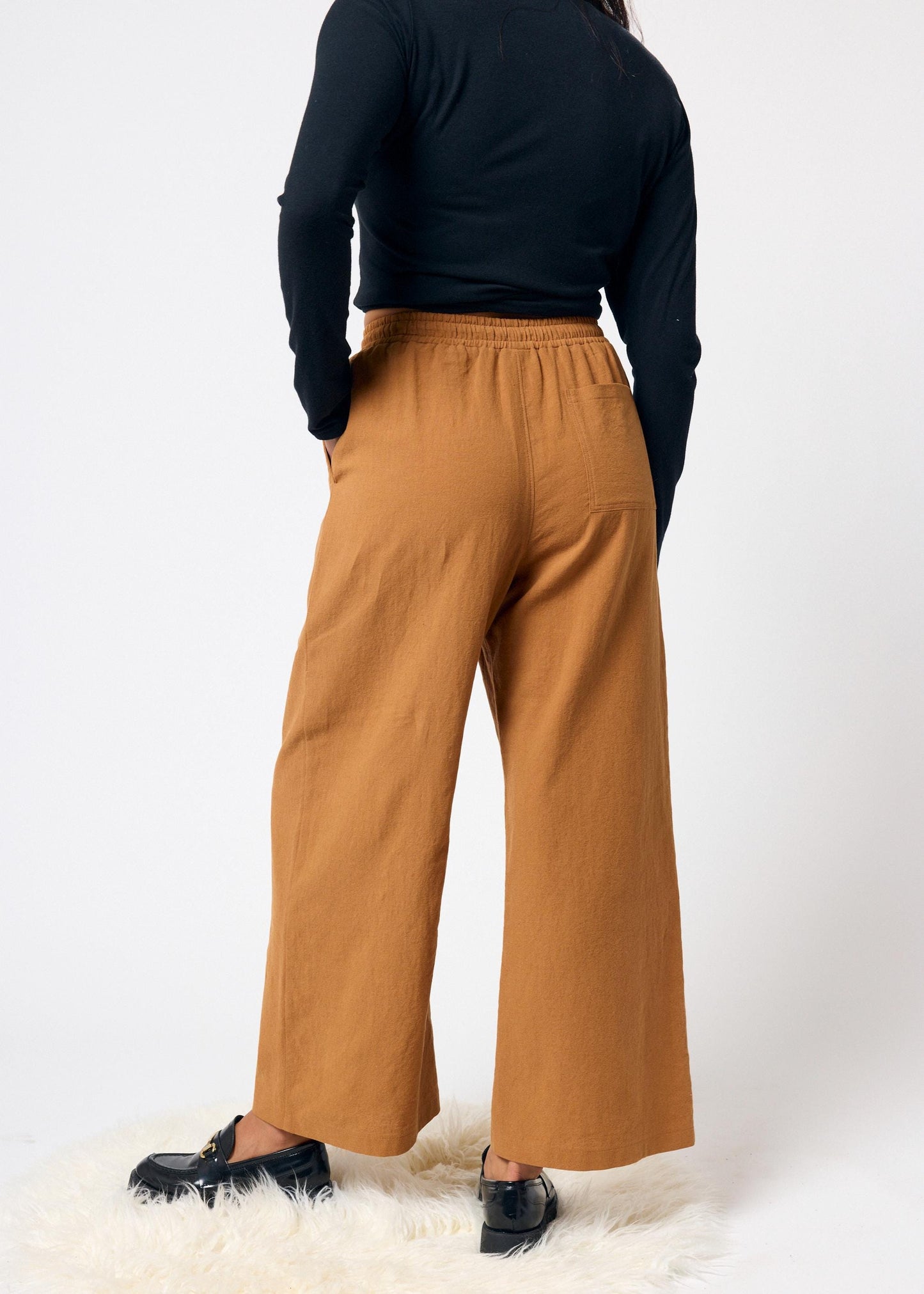 Person wearing mustard yellow wide-leg pants and a black top on a white background