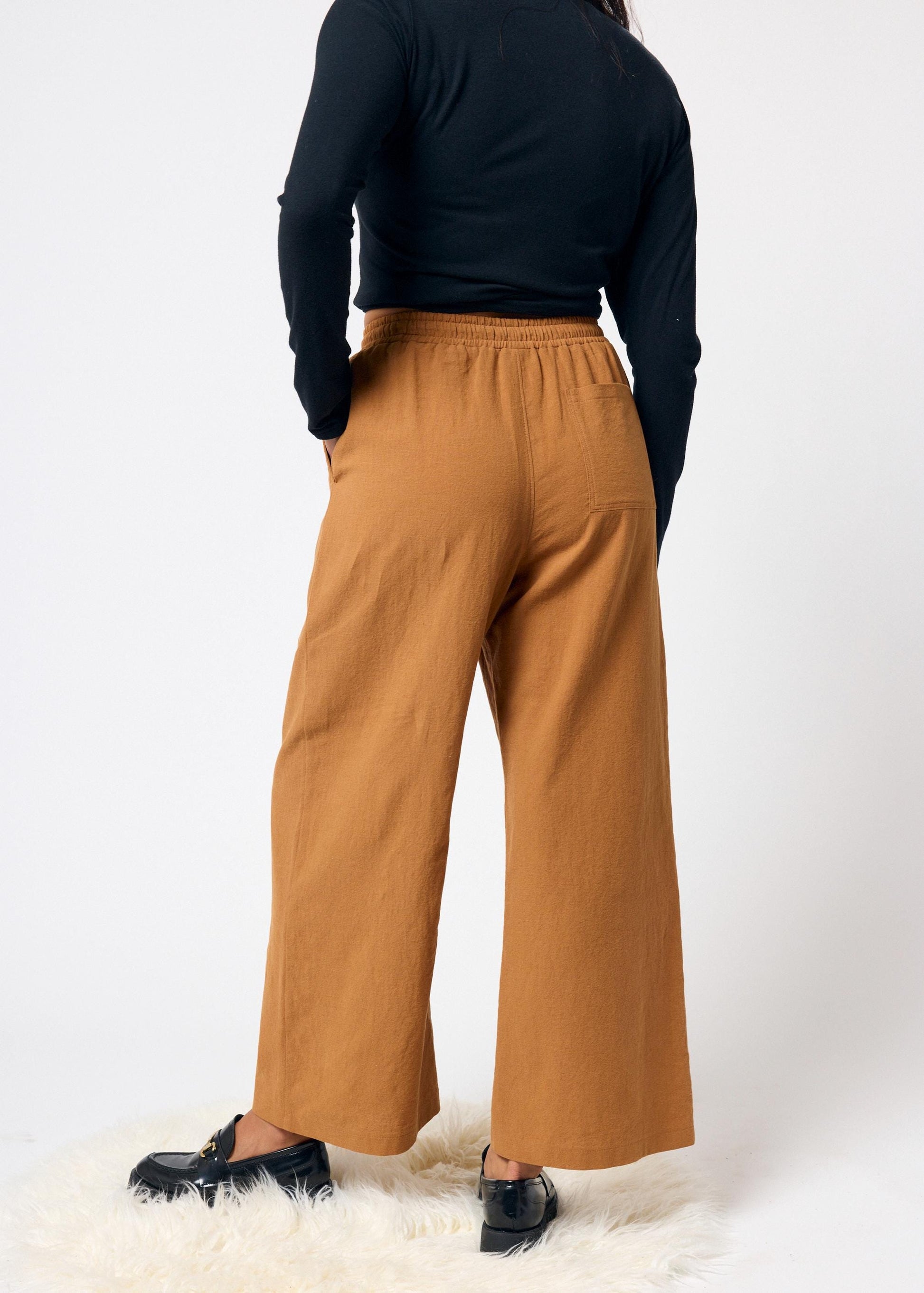 Person wearing mustard yellow wide-leg pants and a black top on a white background