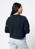 Woman wearing cropped black long sleeve tee shirt with embroidered gray barbed wire design on left arm