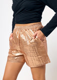 Person wearing bronze metallic shorts and a black top on a white background