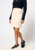 Person wearing a black top and beige denim skirt on a white background