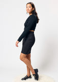 Woman wearing a black shirt and black denim skirt with black shoes on a white background