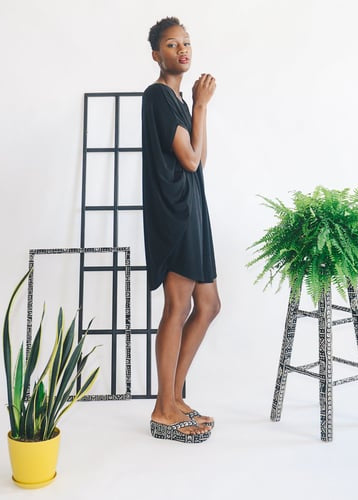woman standing i room with windowpanes and plants, wearing a black dress