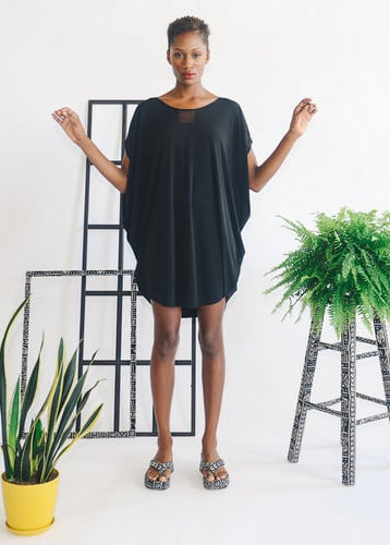 woman wearing black dress, standing in room with plants and windowpanes